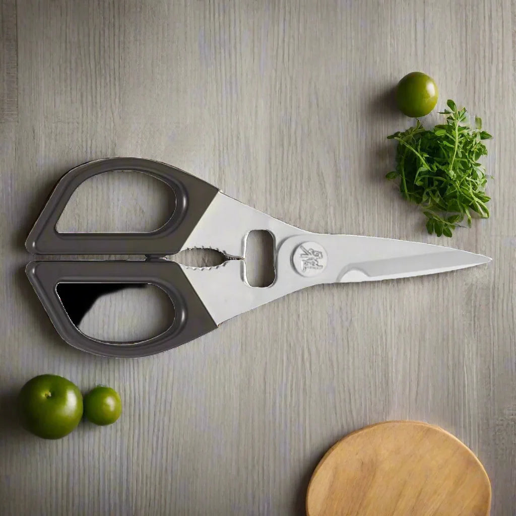 Stainless steel multi-purpose kitchen shears on wooden surface with herbs and green tomatoes