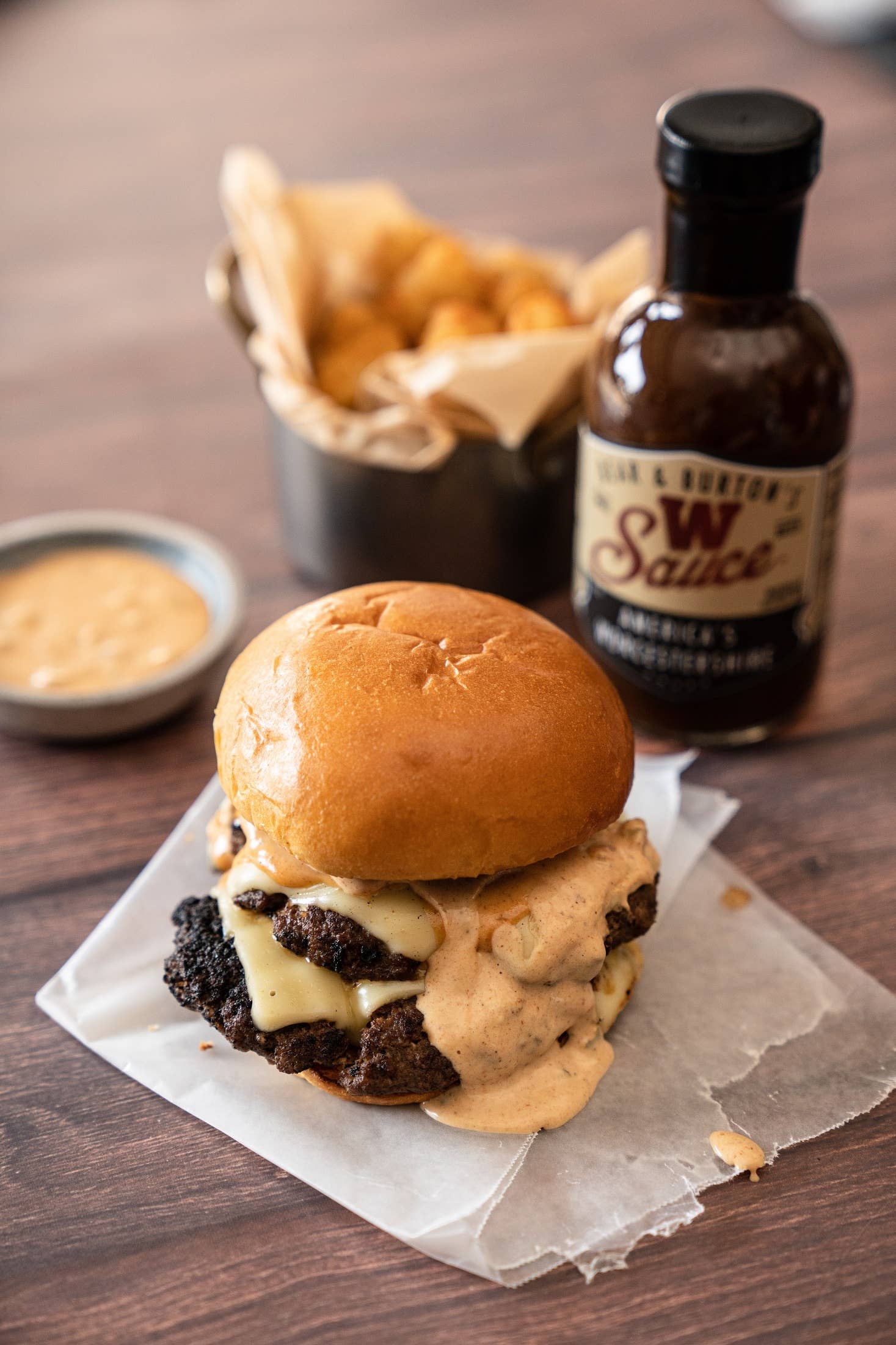 Cheeseburger with creamy sauce on toasted bun, served with tater tots and barbecue sauce bottle