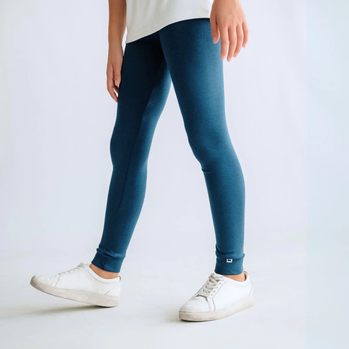 Child wearing teal leggings and white sneakers against a plain background