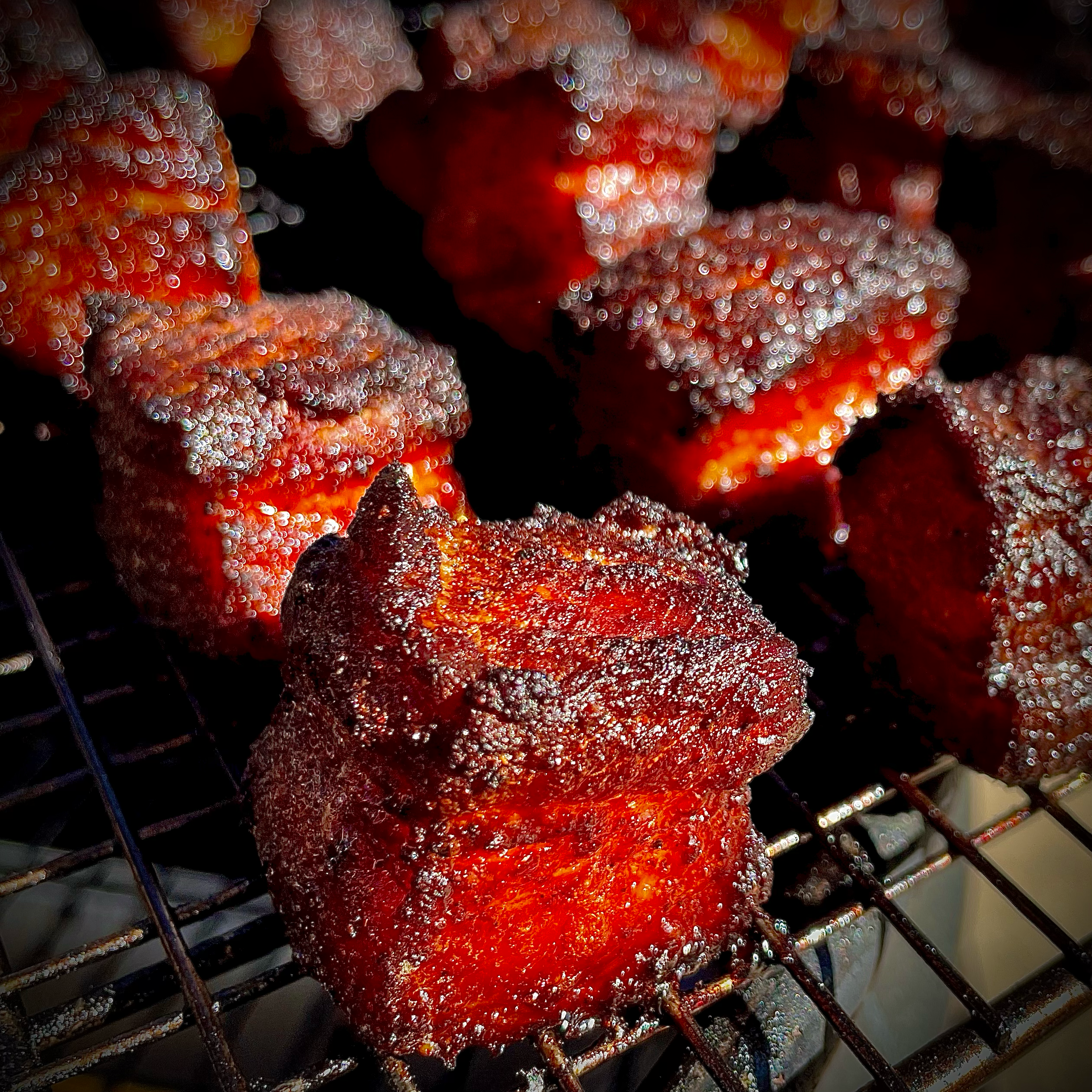 Close-up of smoked pork belly burnt ends on a grill with crispy bark, outdoor BBQ setting