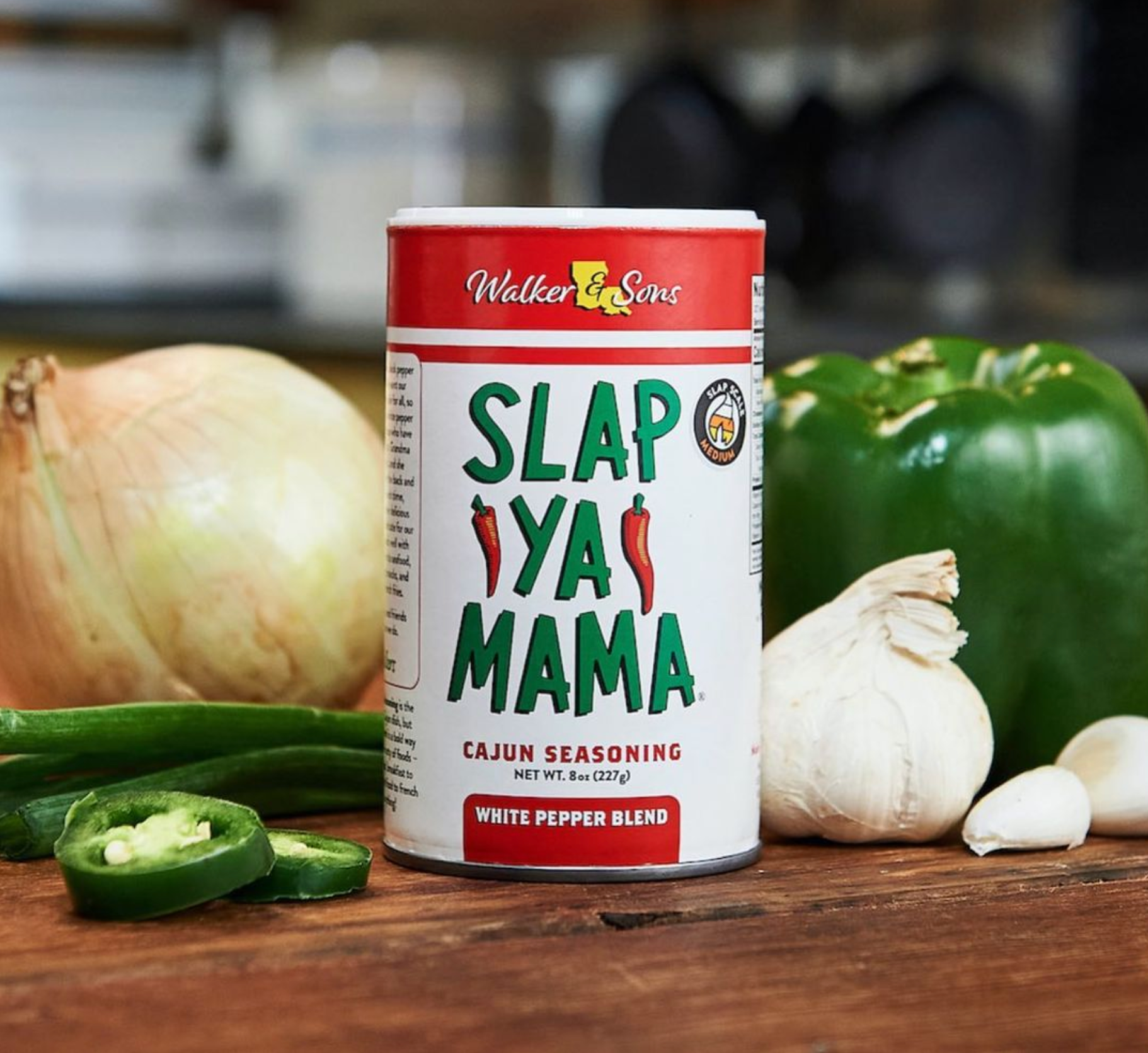 Slap Ya Mama Cajun seasoning can with white pepper blend on a kitchen counter with onion, bell pepper, garlic, and sliced jalapeño.