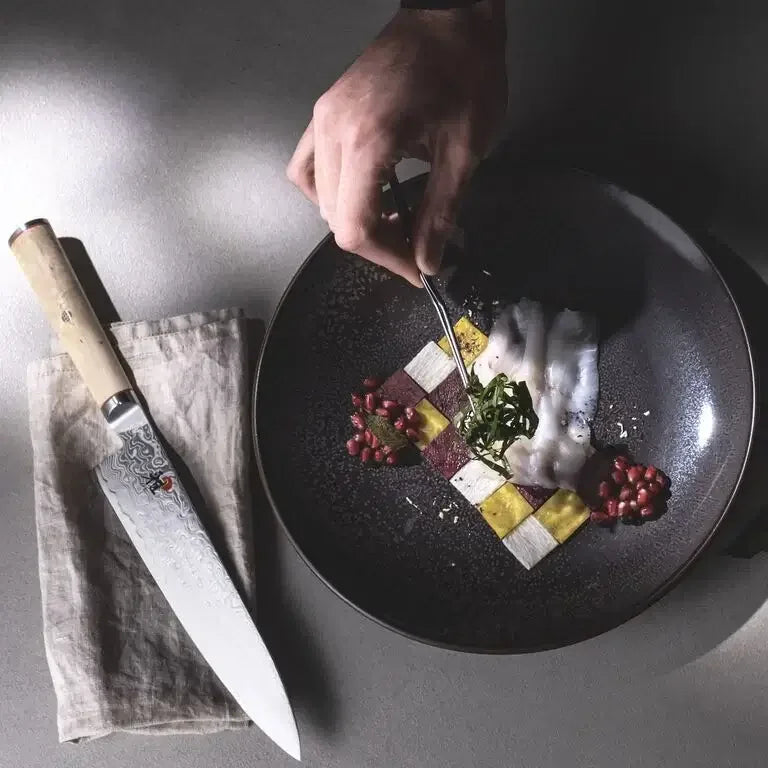 Hand plating gourmet dish with raw fish, pomegranate, and chef knife on linen napkin