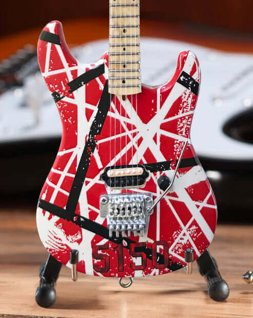 Miniature red electric guitar with white and black stripes, 5150 on body, on wood surface