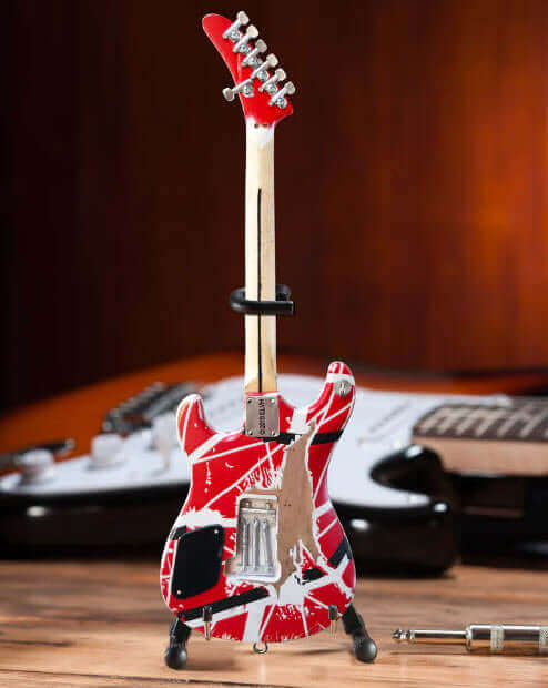 Miniature red and white electric guitar on wooden surface with blurred guitars in background