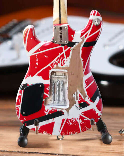 Miniature red electric guitar with white and black stripes on wood surface