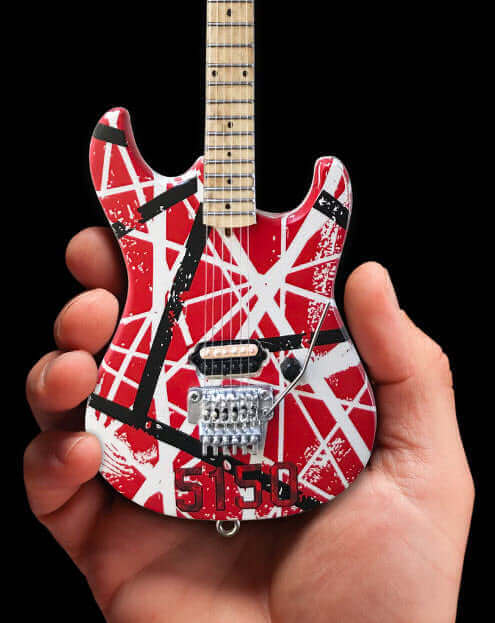 Miniature red electric guitar with white and black stripes held in hand