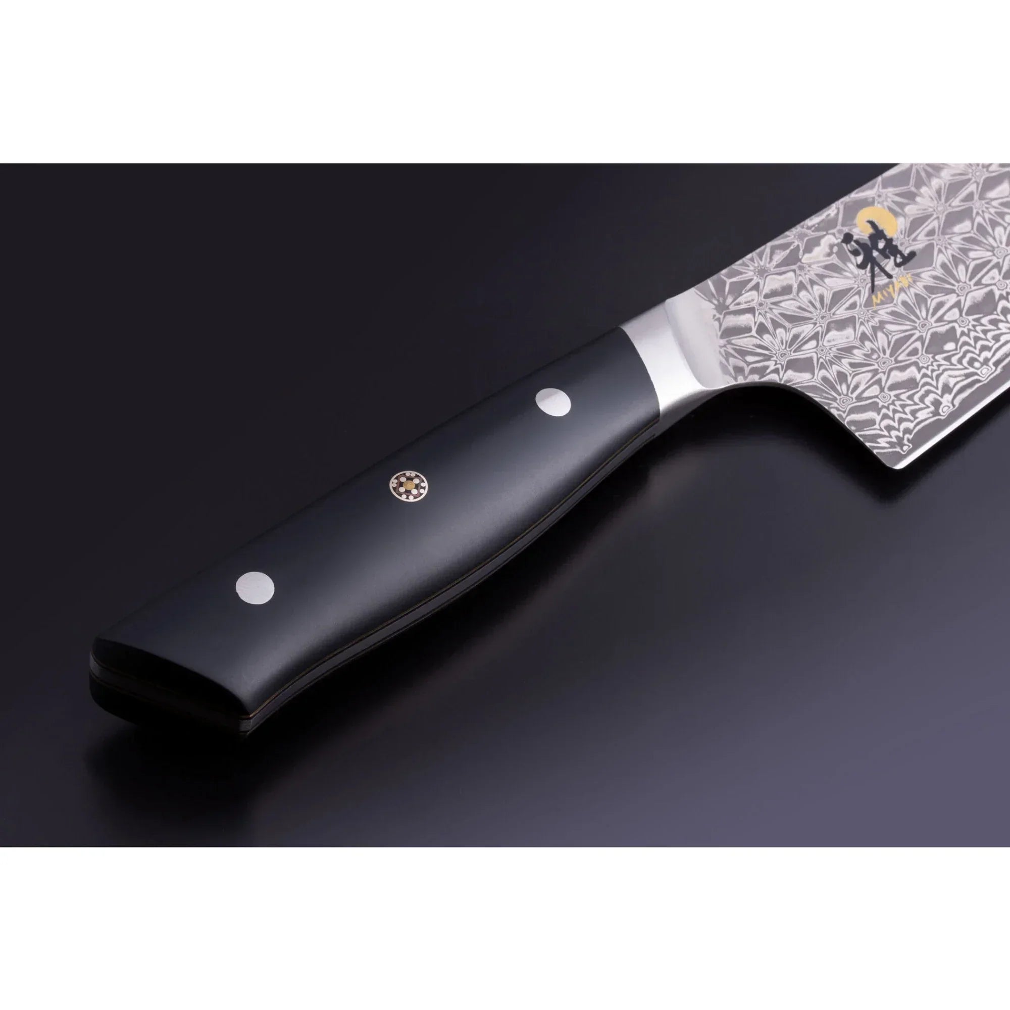 Close-up of a Japanese-style chef's knife with black handle and patterned steel blade