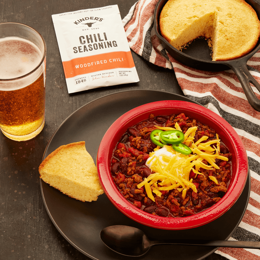 Bowl of chili with cheese, jalapeños, cornbread, beer, and chili seasoning packet