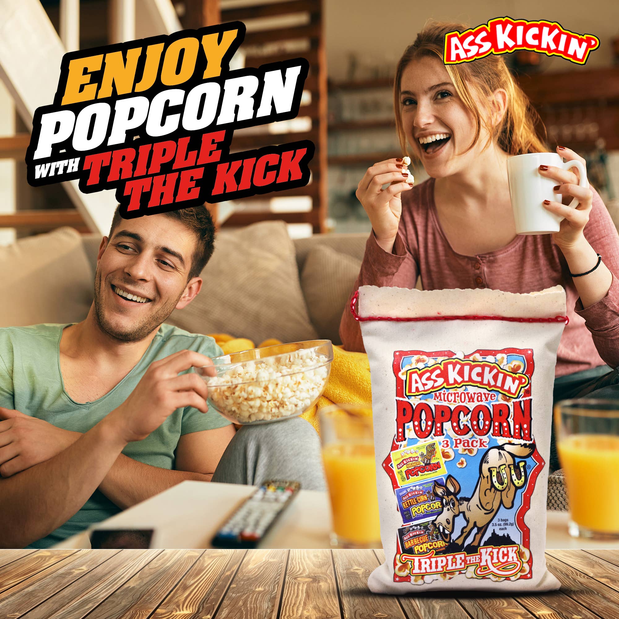 Couple enjoying spicy microwave popcorn on a couch with drinks and TV remote nearby.