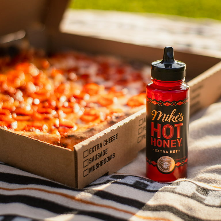 Pepperoni pizza in box with bottle of Mike's Hot Honey extra hot on picnic blanket outdoors