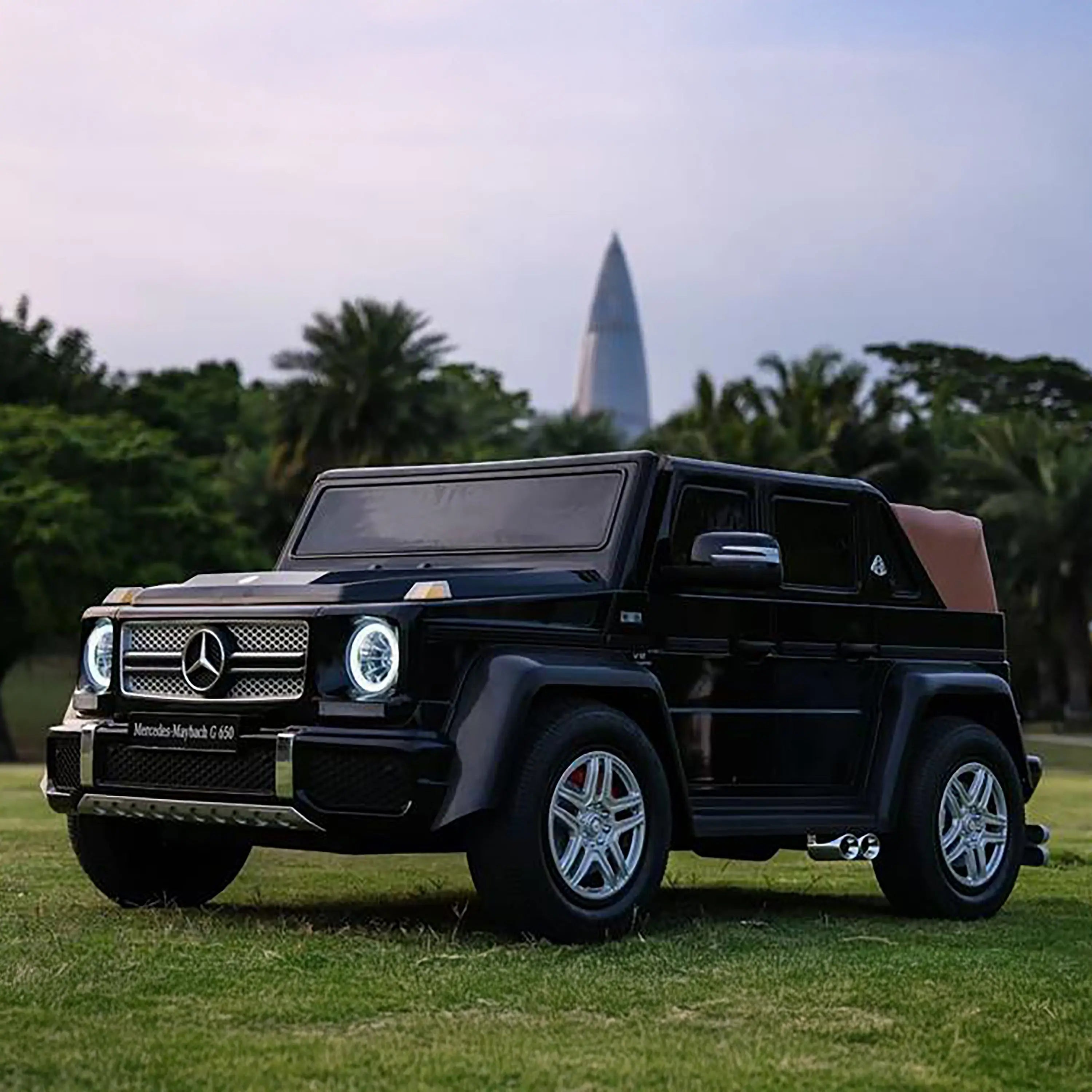 Black toy SUV with headlights on, parked on grass with trees and a tall building in background