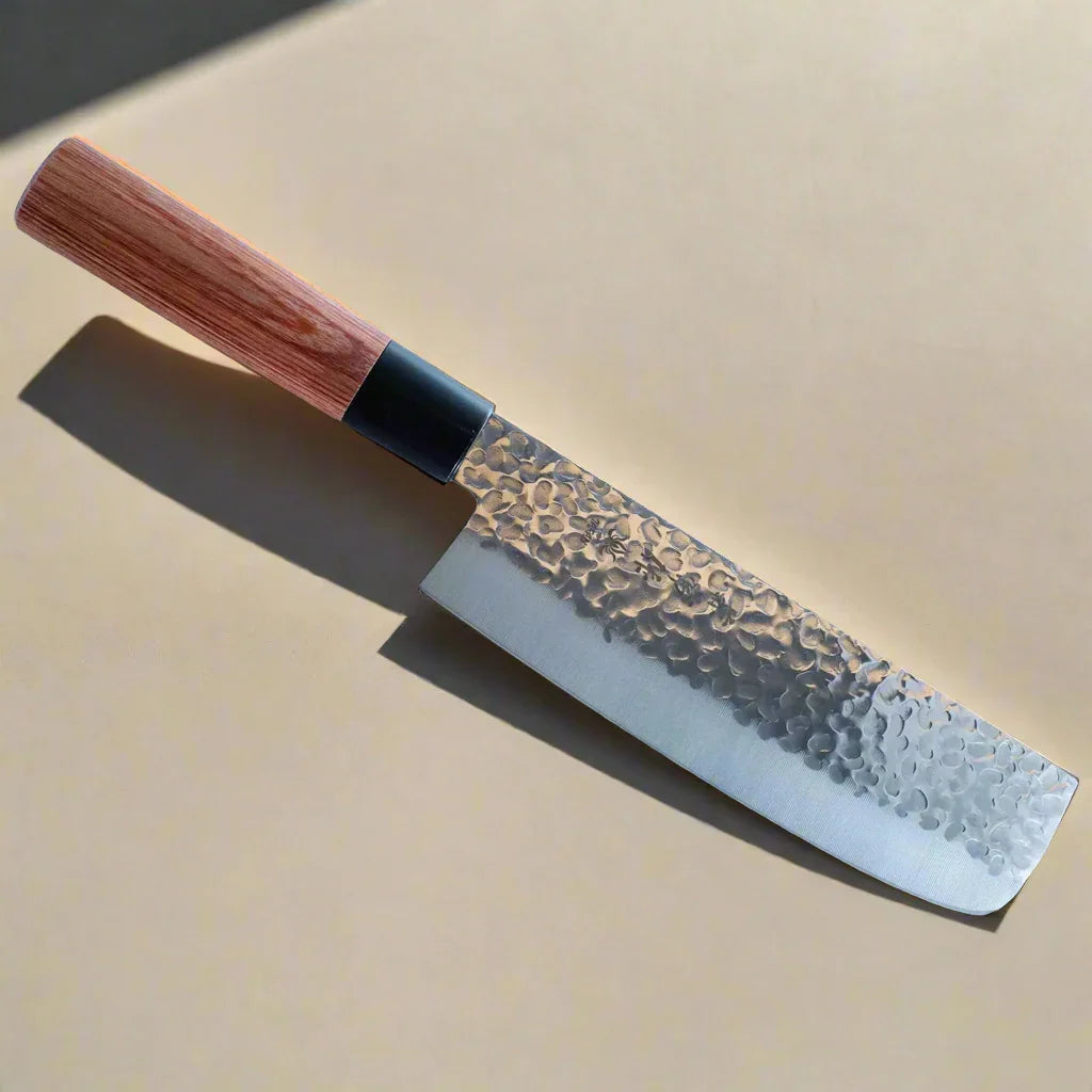 Japanese-style hammered steel kitchen knife with wooden handle on tan background