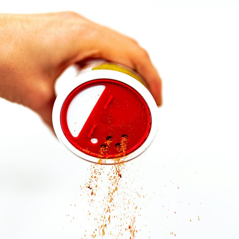 Hand pouring seasoning or spice from red-lidded shaker, camping cooking accessory