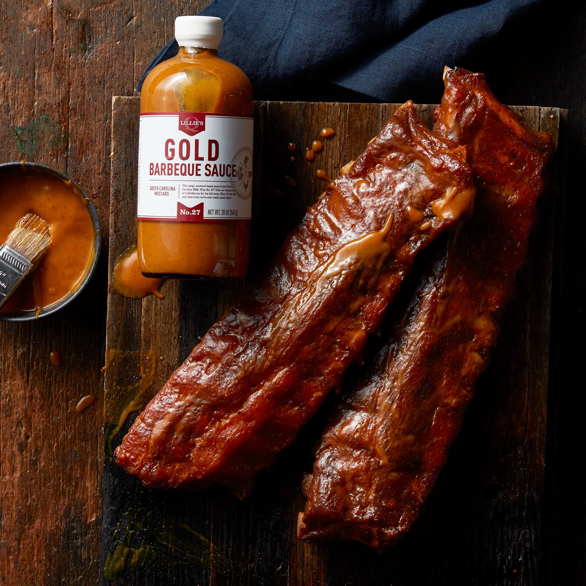 Smoked pork ribs with gold barbecue sauce and basting brush on rustic wooden board