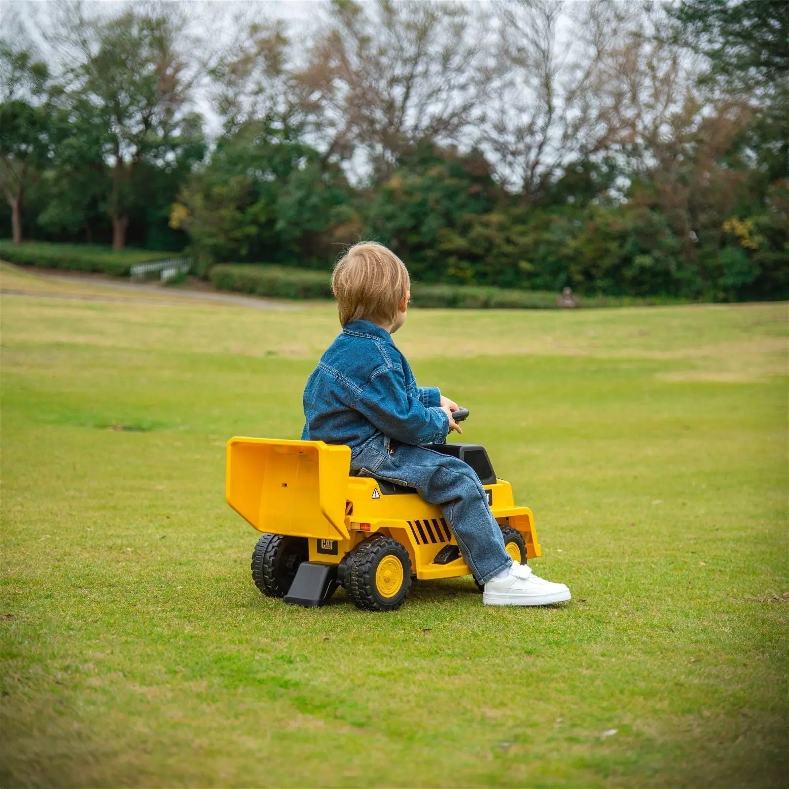 Child riding yellow dump truck ride-on toy outdoors on green grass