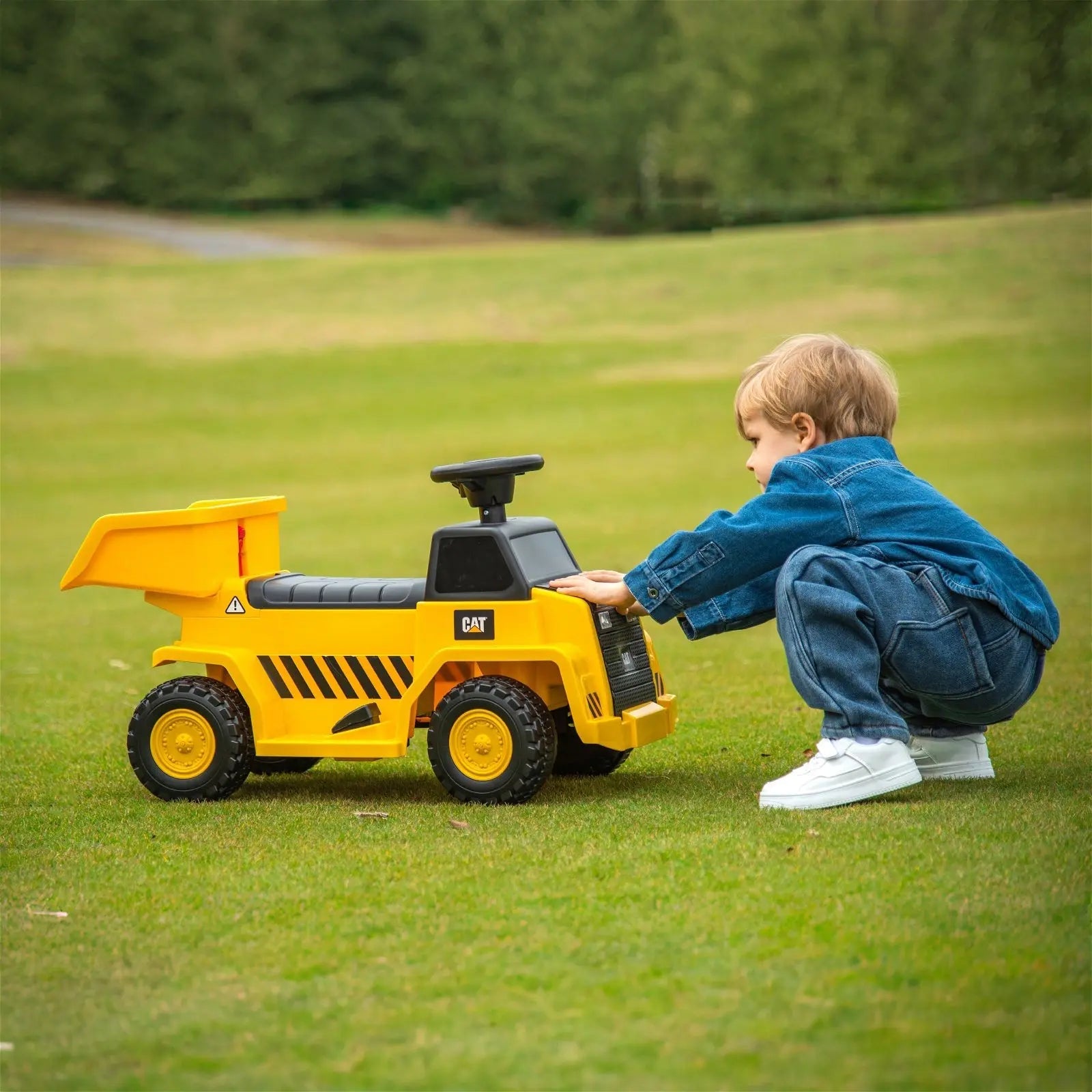 Child playing outdoors with yellow ride-on CAT dump truck toy on green grass