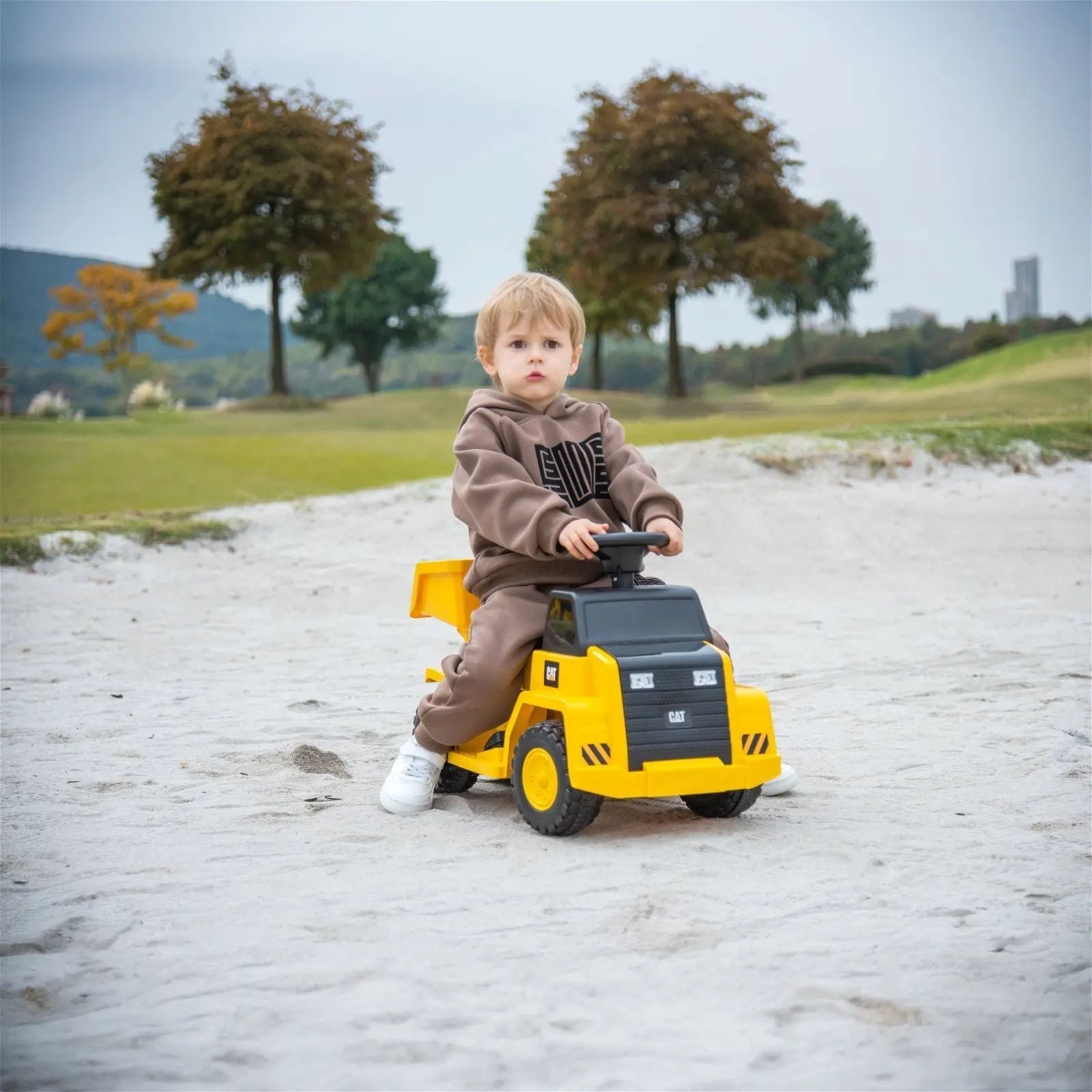 Child riding yellow CAT dump truck ride-on toy on sandy outdoor area