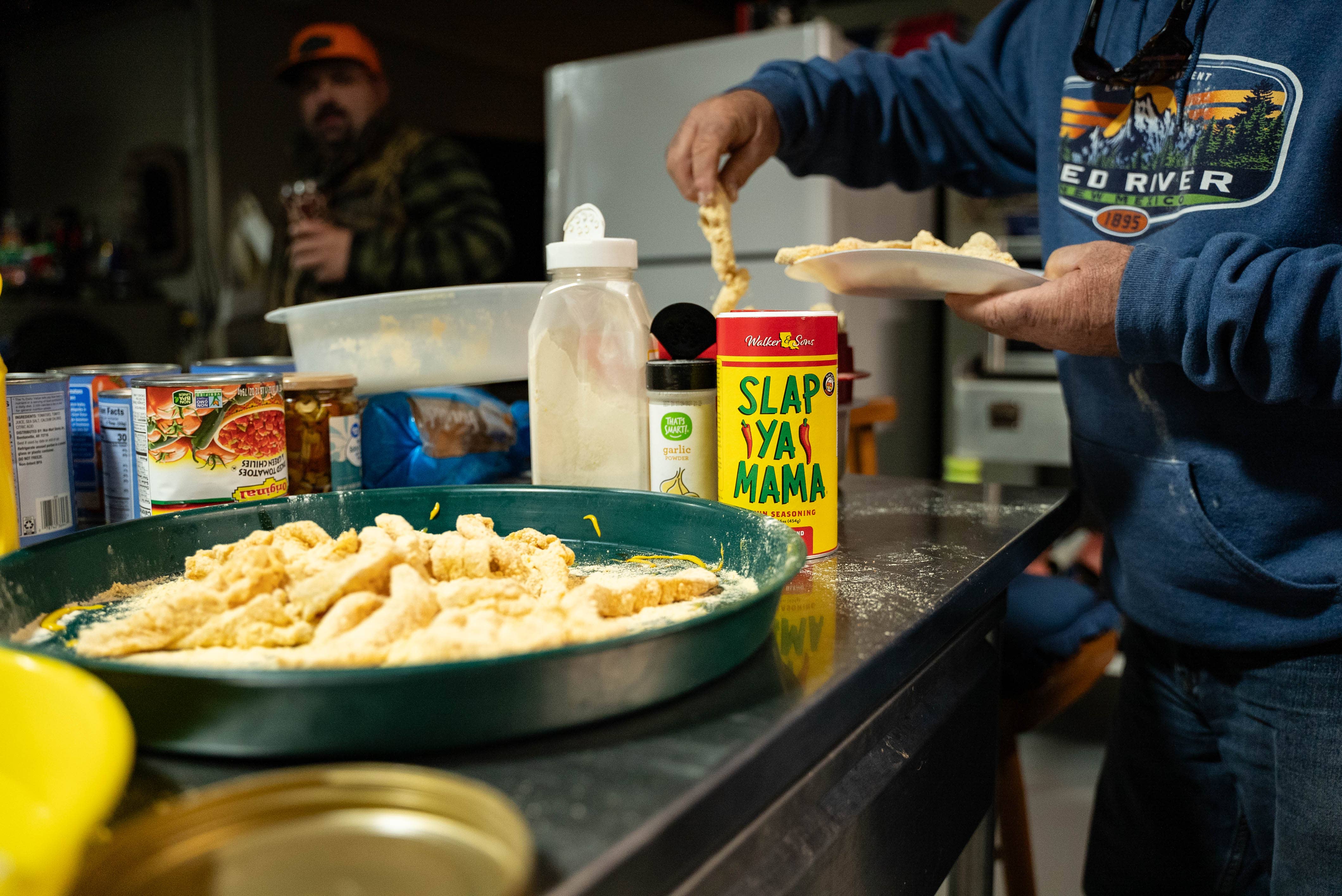Preparing seasoned breaded meat in a rustic kitchen with outdoor camping supplies