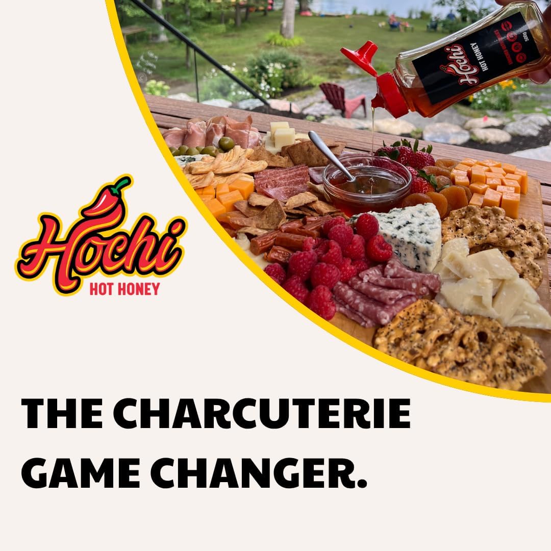 Bottle of Hochi hot honey drizzled over charcuterie board with cheese, meats, fruit, and crackers outdoors.