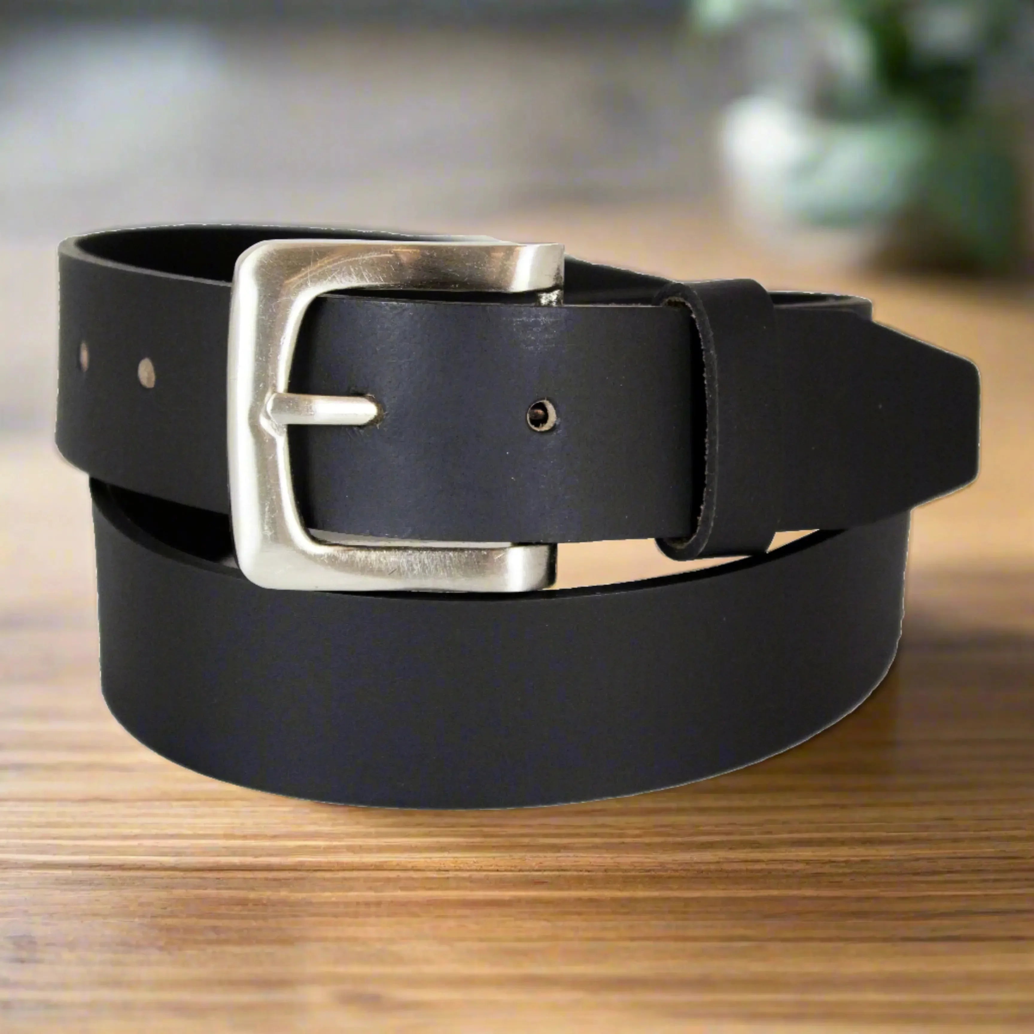 Men's black smooth leather belt with removable silver buckle on wooden surface