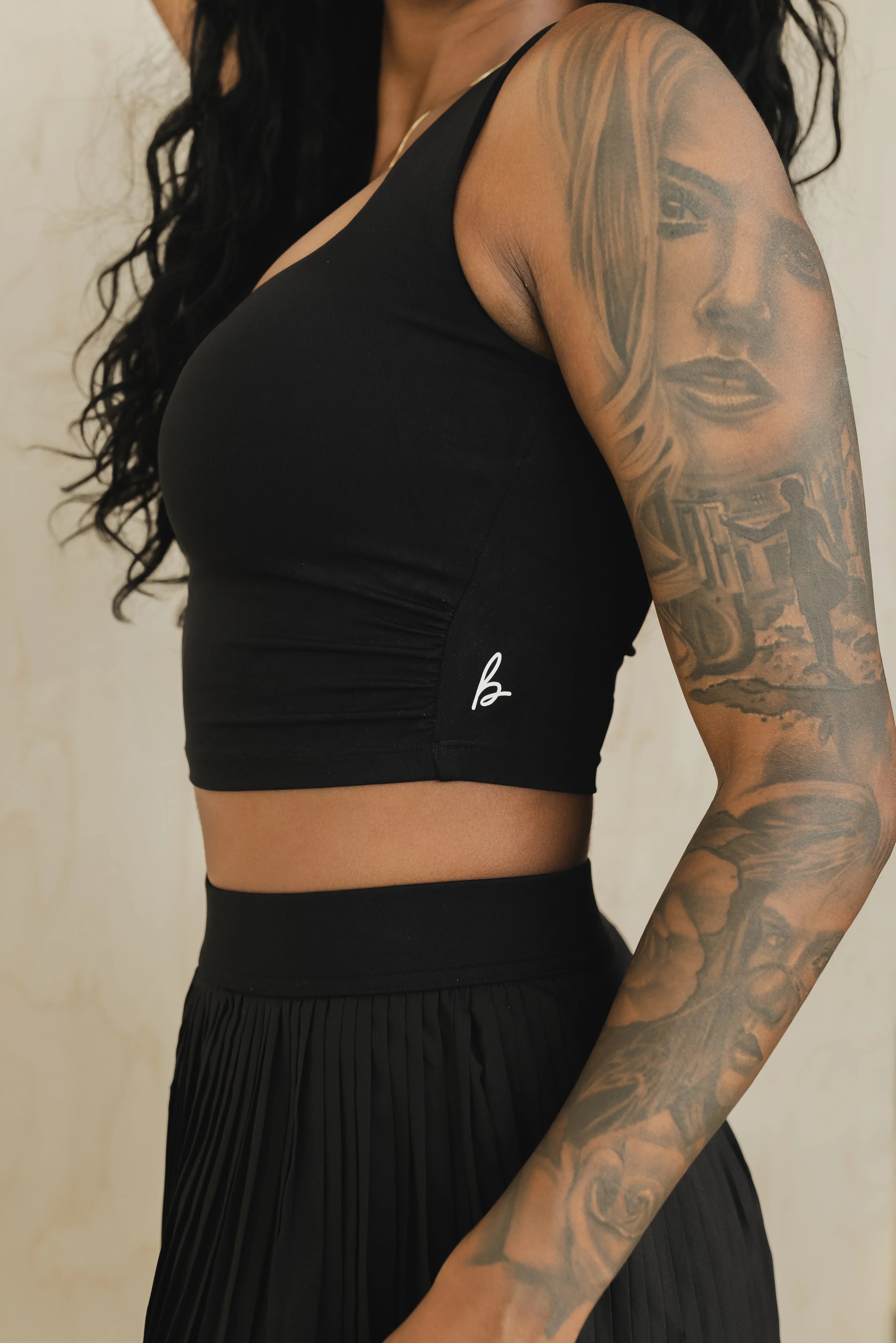 Woman in black crop top and pleated skirt showing detailed portrait tattoo sleeve