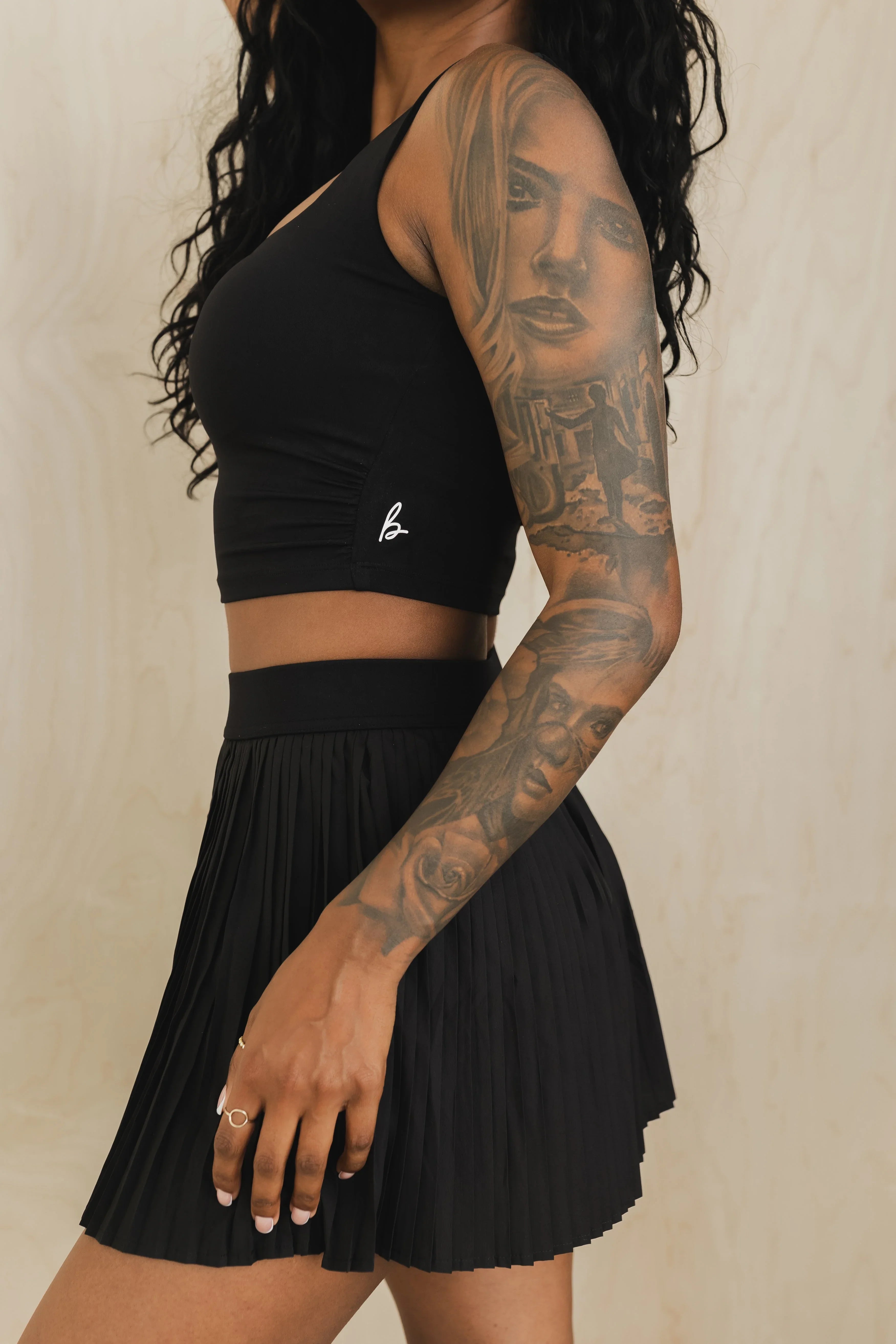 Woman in black crop top and pleated skirt with detailed sleeve tattoos