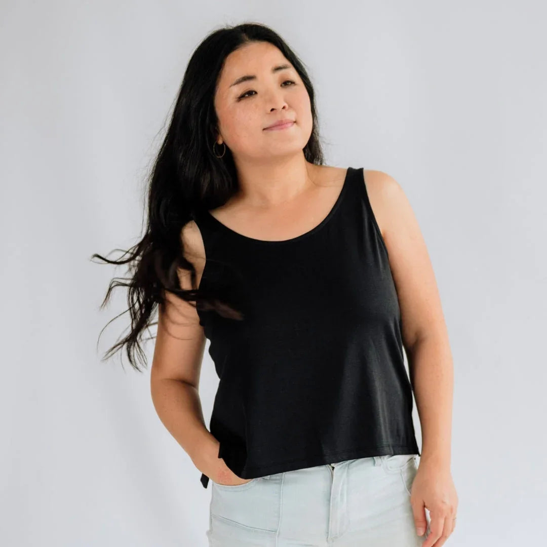 Woman wearing black bamboo cropped tank top and light jeans against plain background