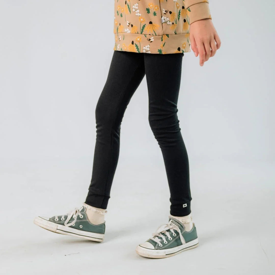 Youth wearing black bamboo leggings and green sneakers, floral top, studio background