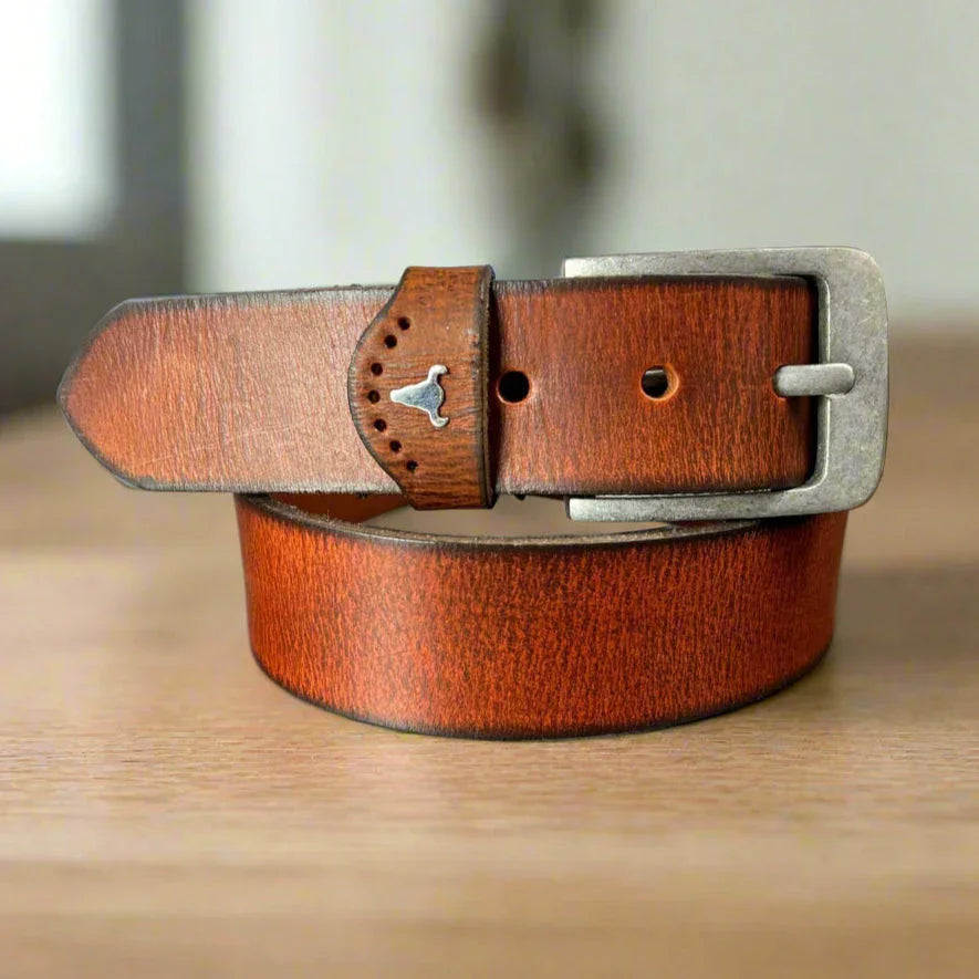 Brown leather belt with silver buckle and bull head detail on wooden surface