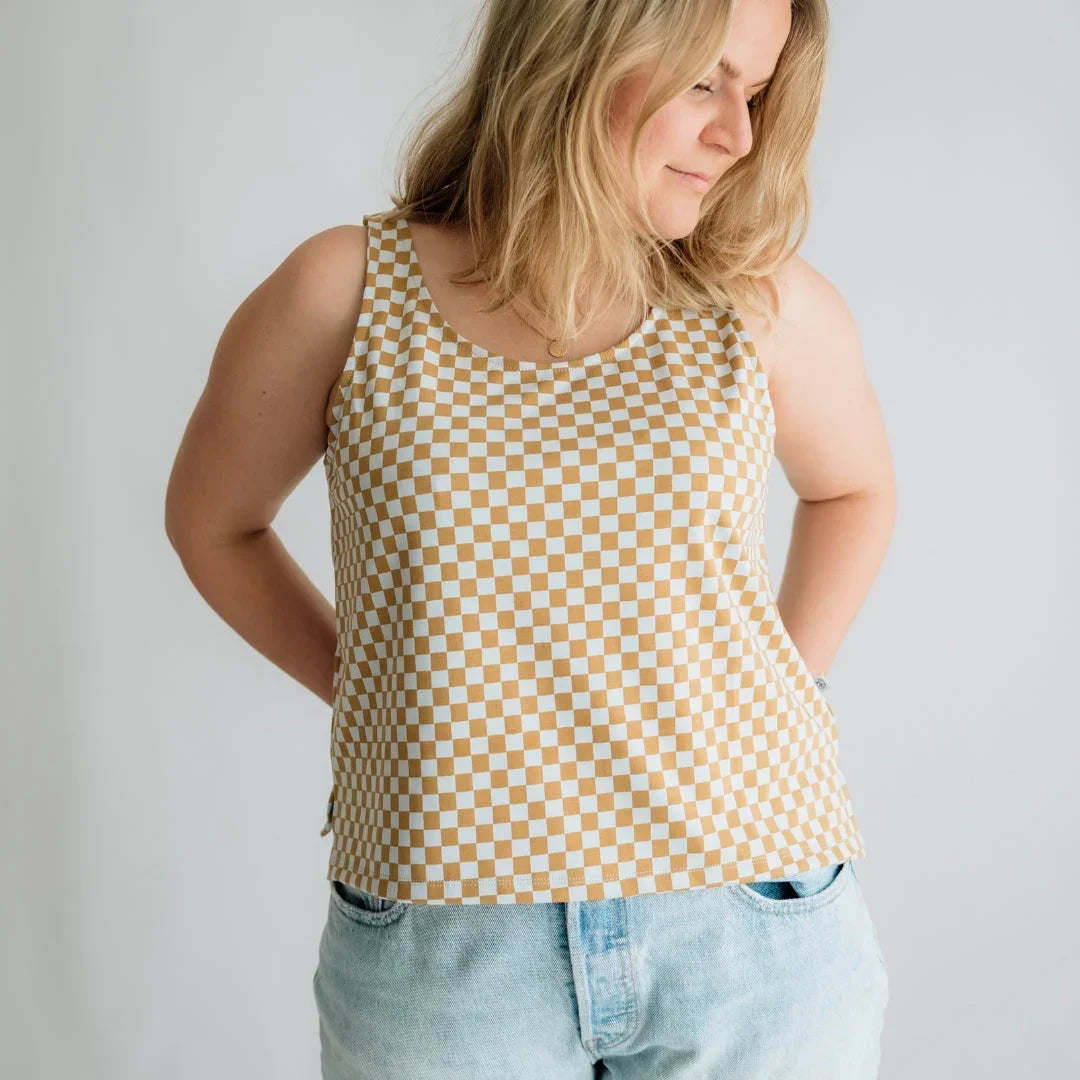 Woman wearing beige and white checkered tank top and light blue jeans on plain background