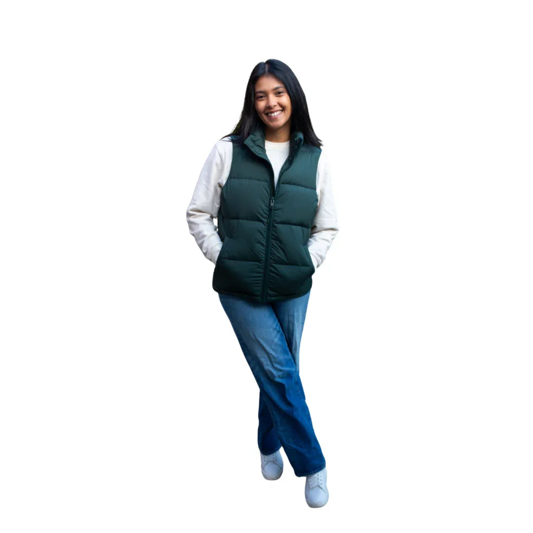 Woman wearing green puffer vest, white sweater, blue jeans, and white sneakers on white background