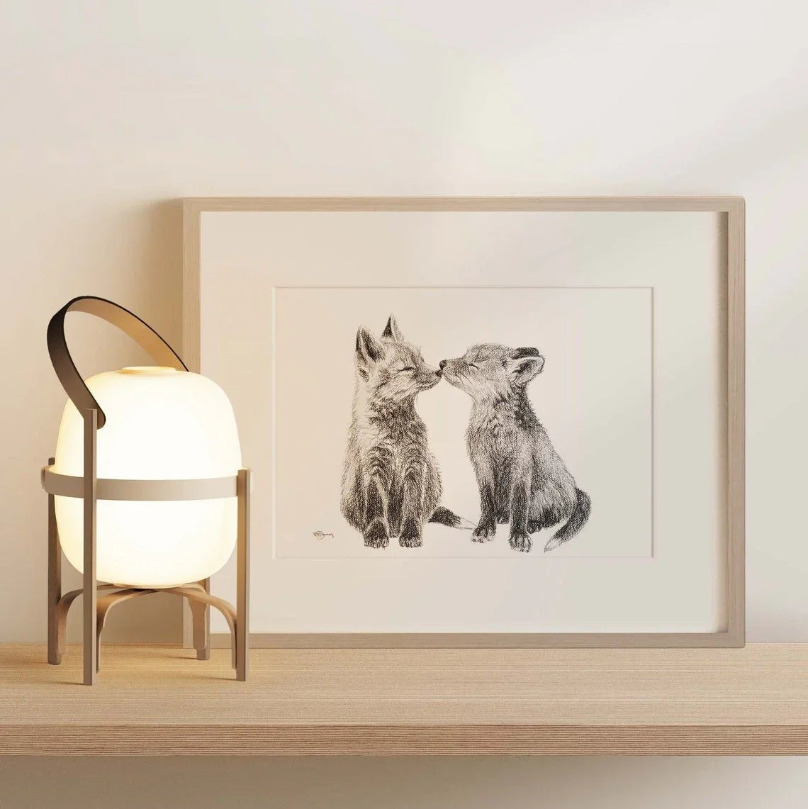 Framed sketch of two baby foxes on a shelf beside a modern table lamp