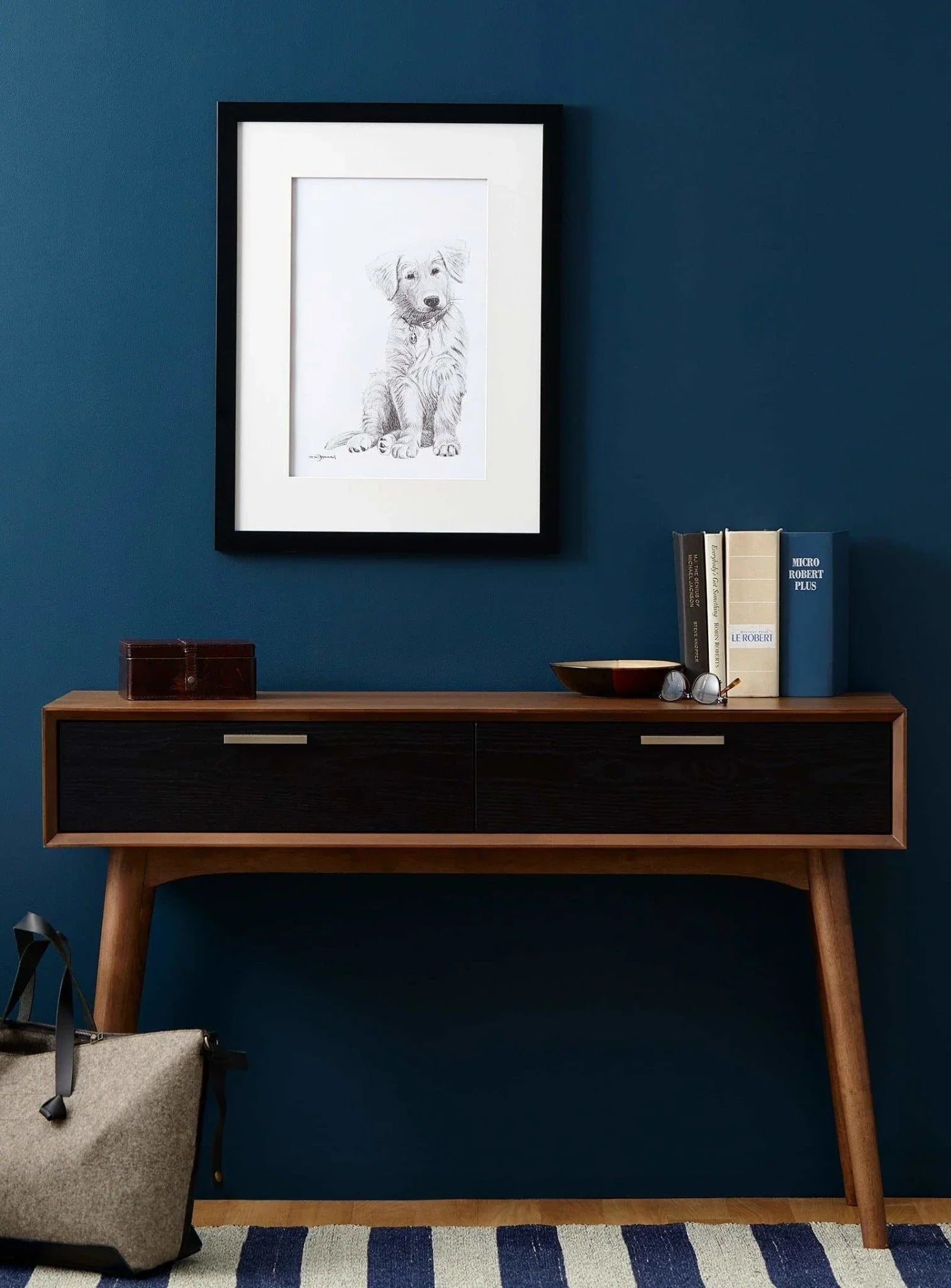 Framed golden retriever puppy sketch on blue wall above mid-century wood console table