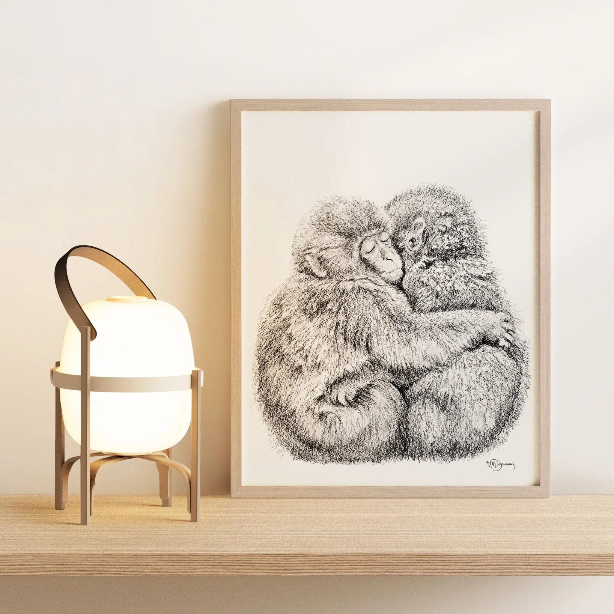 Framed sketch of two hugging monkeys beside a modern table lamp on a wooden shelf.