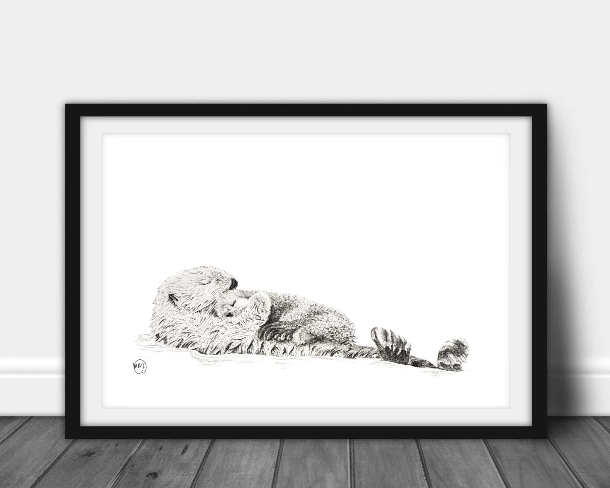 Framed black and white illustration of a sea otter cuddling her pup, displayed on wooden floor