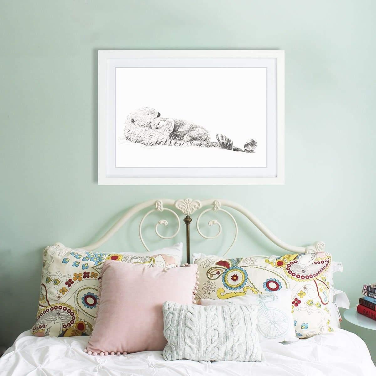 Framed sea otter and cub drawing above vintage bed with colorful pillows in cozy bedroom.