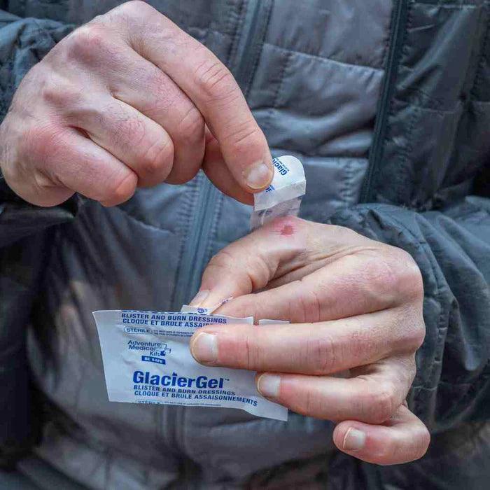 Person applying GlacierGel blister and burn dressing to hand outdoors, closeup view.