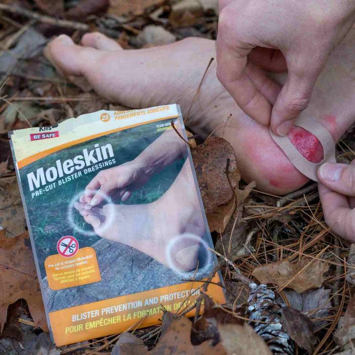 Applying Moleskin blister dressing to foot outdoors on forest floor with product packaging