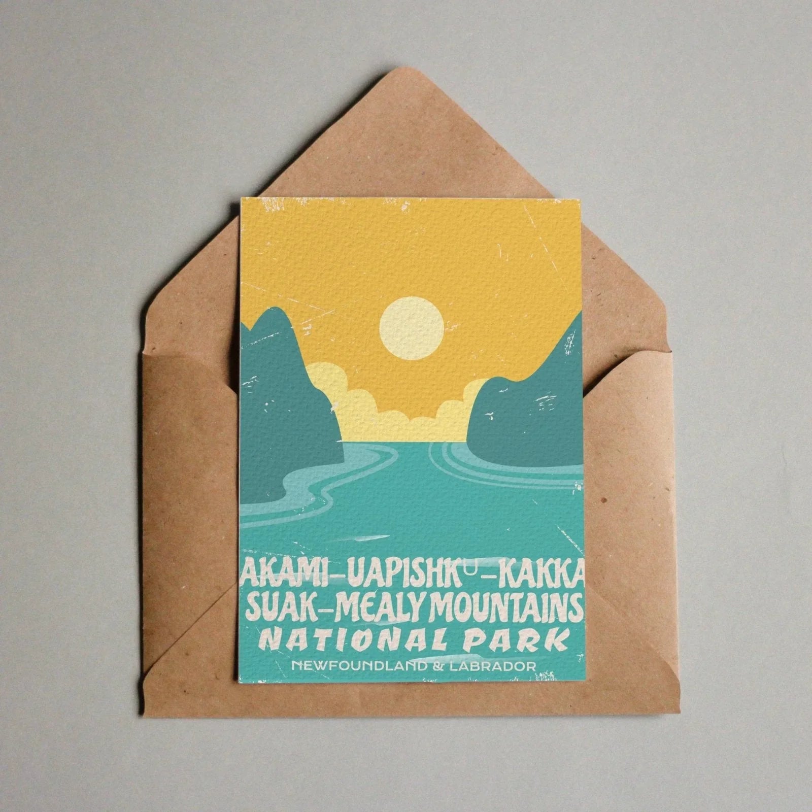 Akami-Uapishku-KakKasuak-Mealy Mountains National Park postcard with stylized sun, mountains, and water in an envelope.