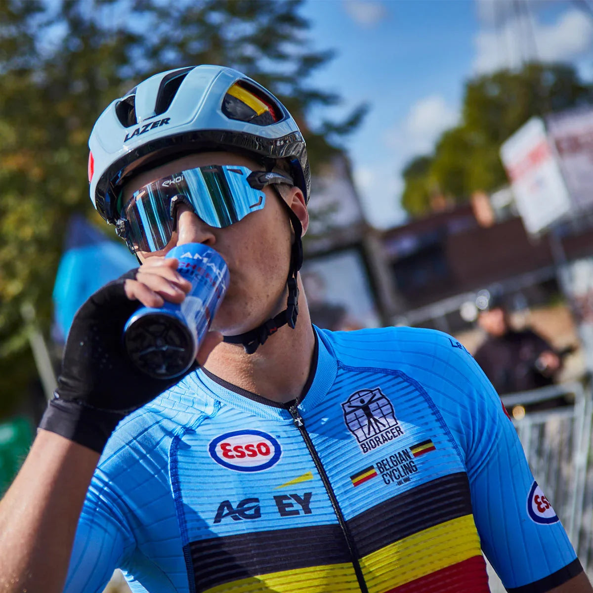 Belgian cyclist in blue jersey and helmet drinking cherry juice outdoors
