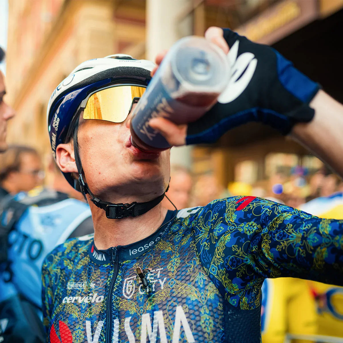 Cyclist in patterned jersey and helmet drinking cherry juice from sports bottle outdoors