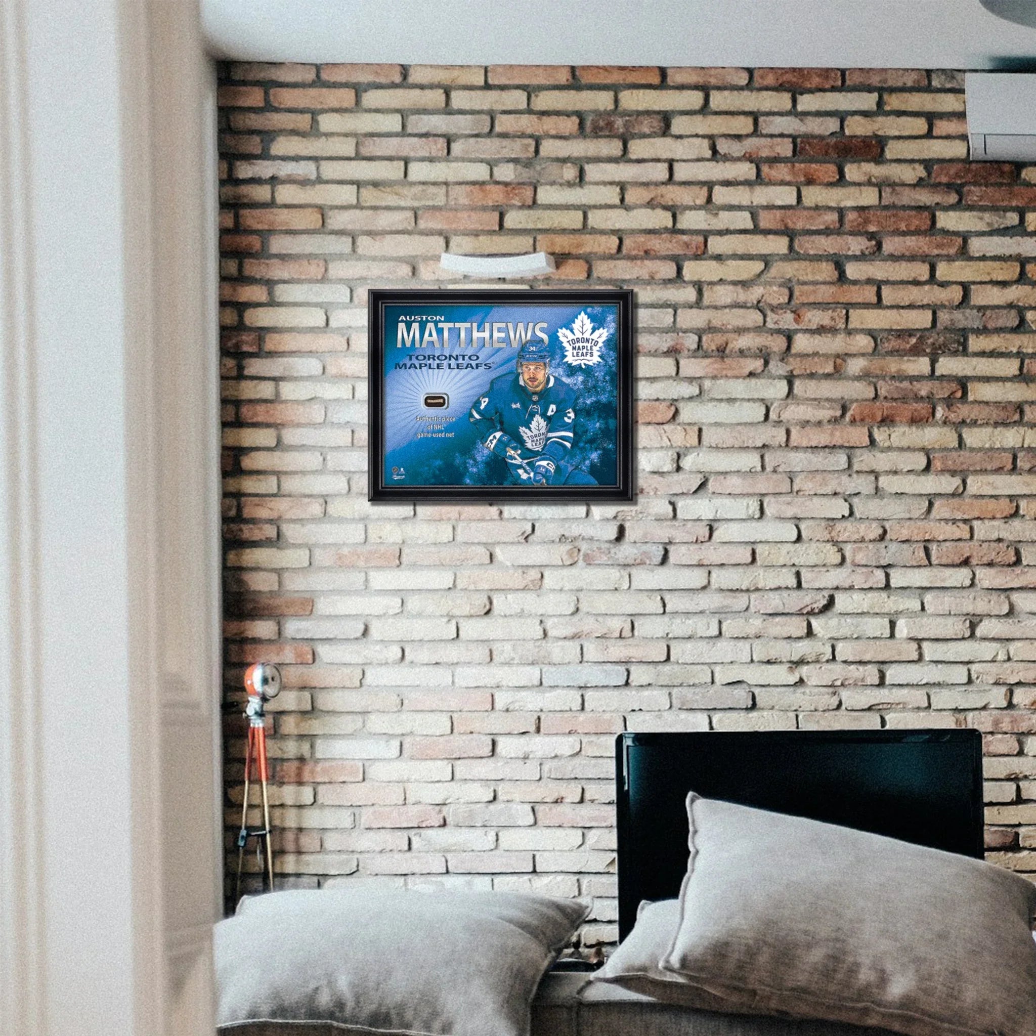 Framed Toronto Maple Leafs Auston Matthews hockey memorabilia on brick wall above sofa.