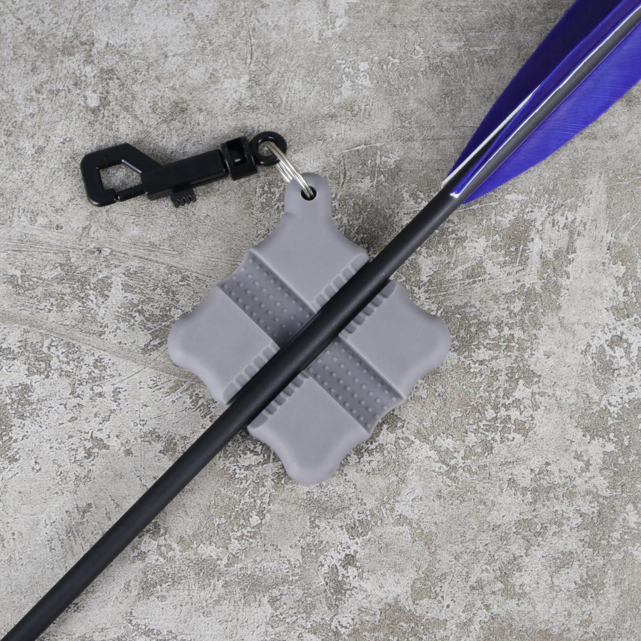 Gray archery flex arrow puller with black carabiner and purple-feathered arrow on concrete