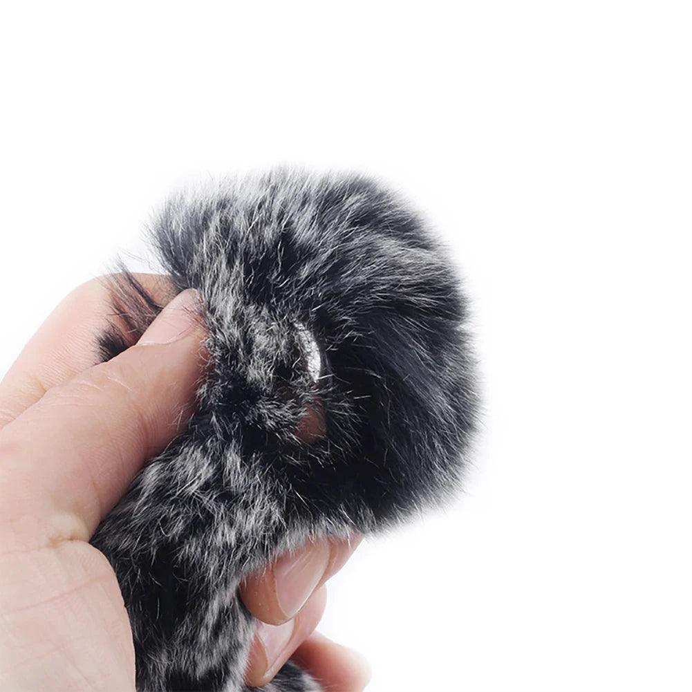 Hand holding black and white fur archery string silencer for recurve bow.