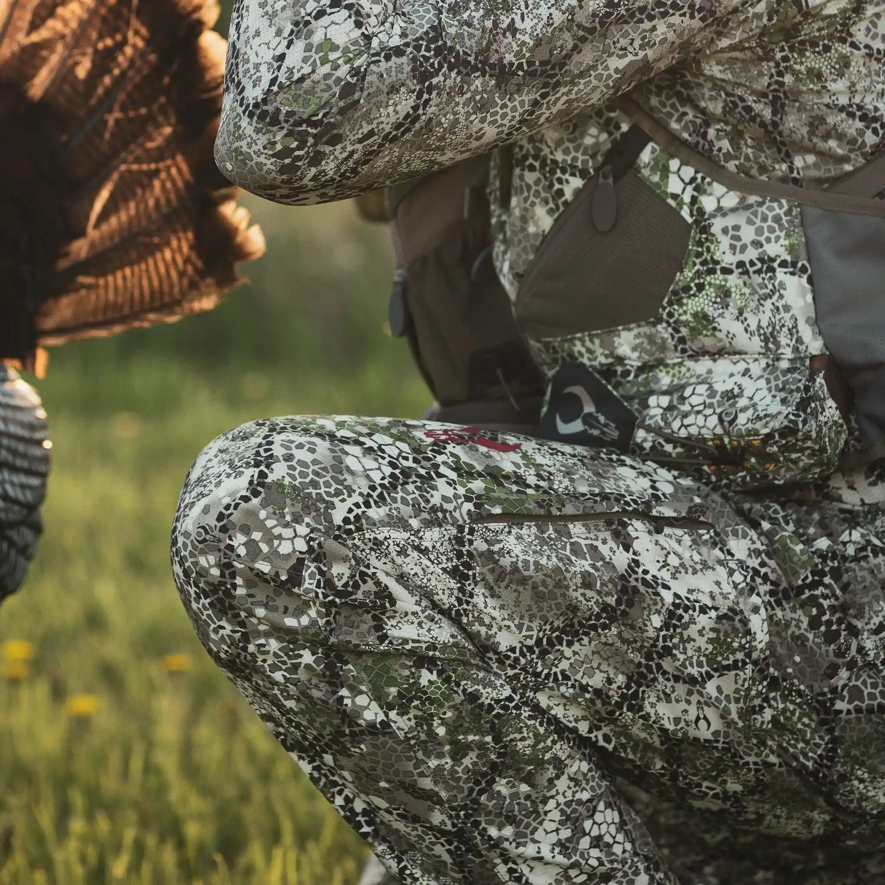 Person kneeling outdoors in Badlands Andaire camo hunting pants and gear, grass background