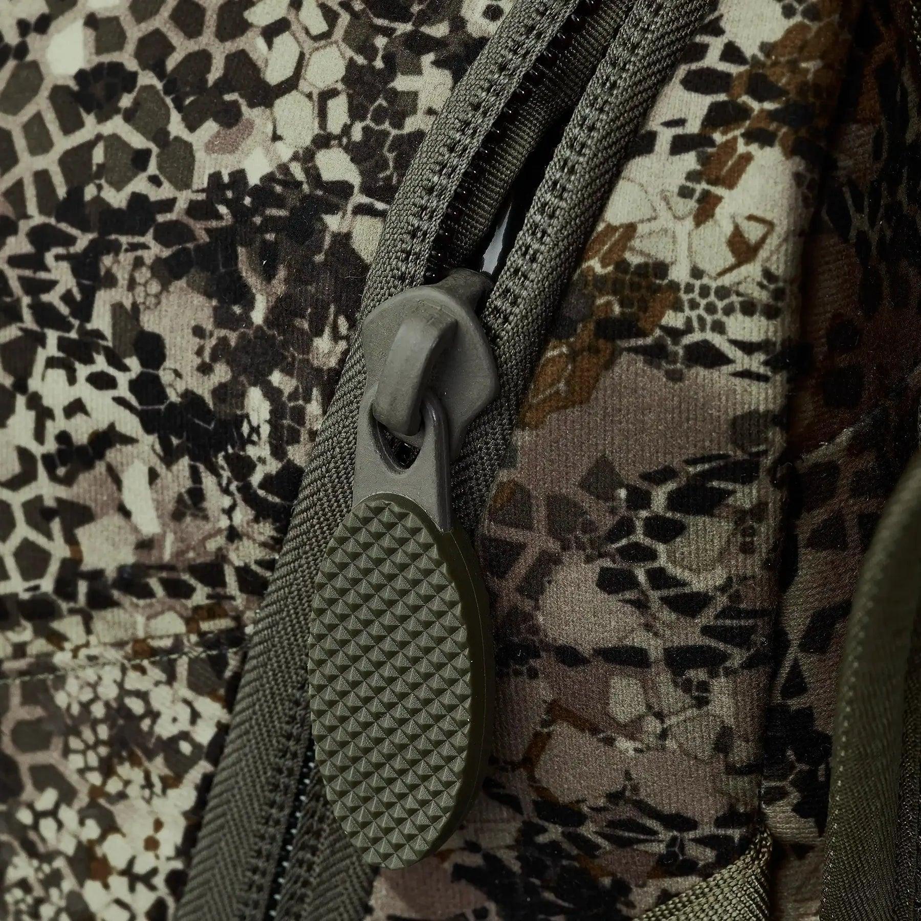 Close-up of camo backpack zipper with textured pull tab, outdoor gear detail
