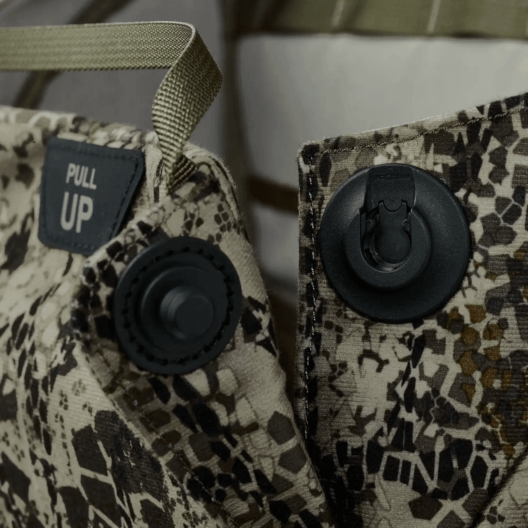 Close-up of camo fabric panel with pull tab, snap fasteners, and PULL UP label