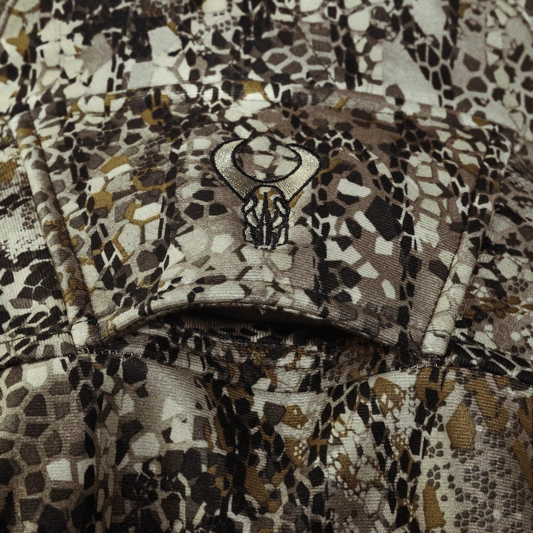 Camo shirt closeup with brown, tan, and black pattern and embroidered horned skull patch