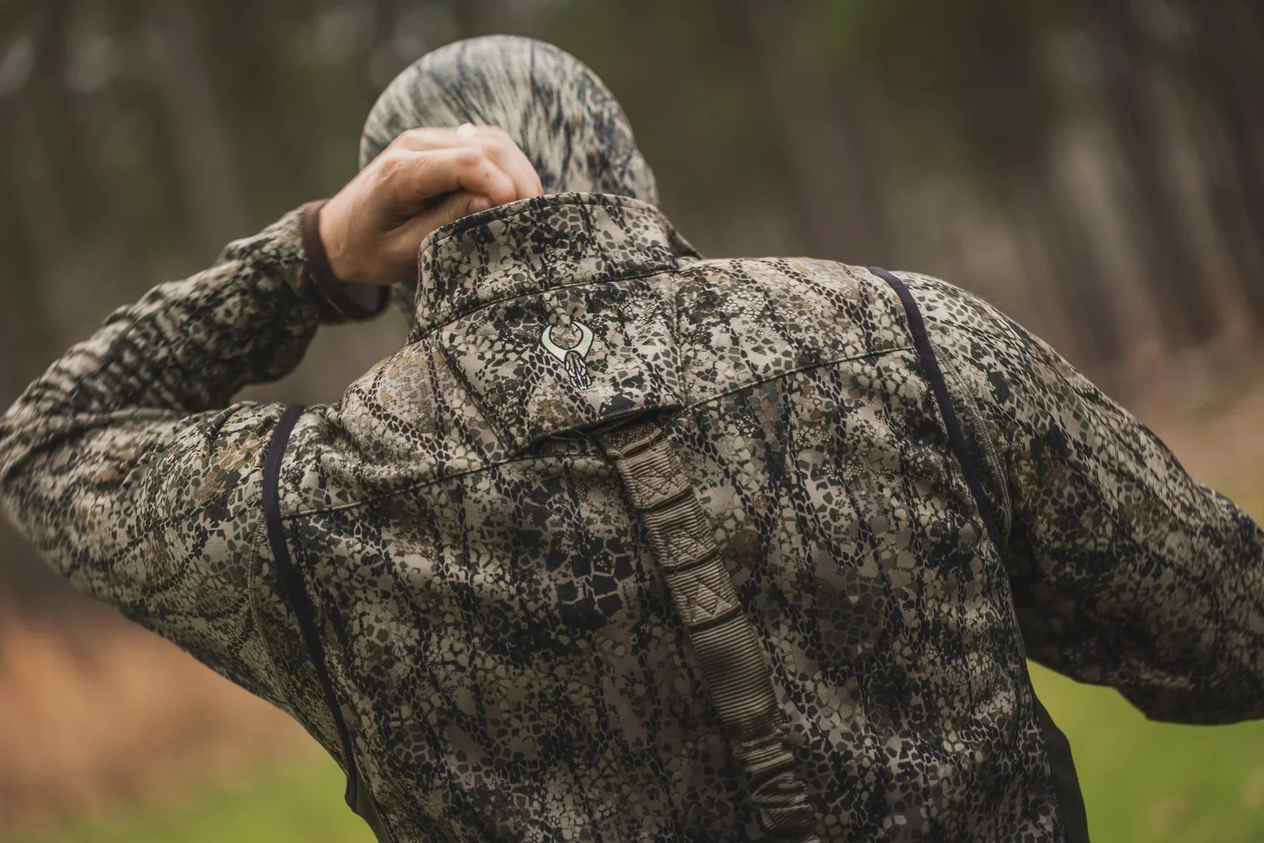 Person in camouflage hunting jacket and hood outdoors in forest setting