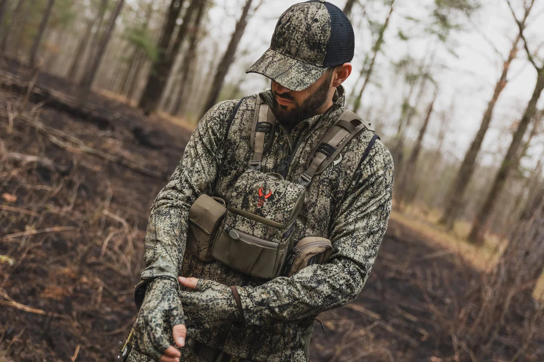 Hunter in camo gear and chest pack in a woodland forest setting